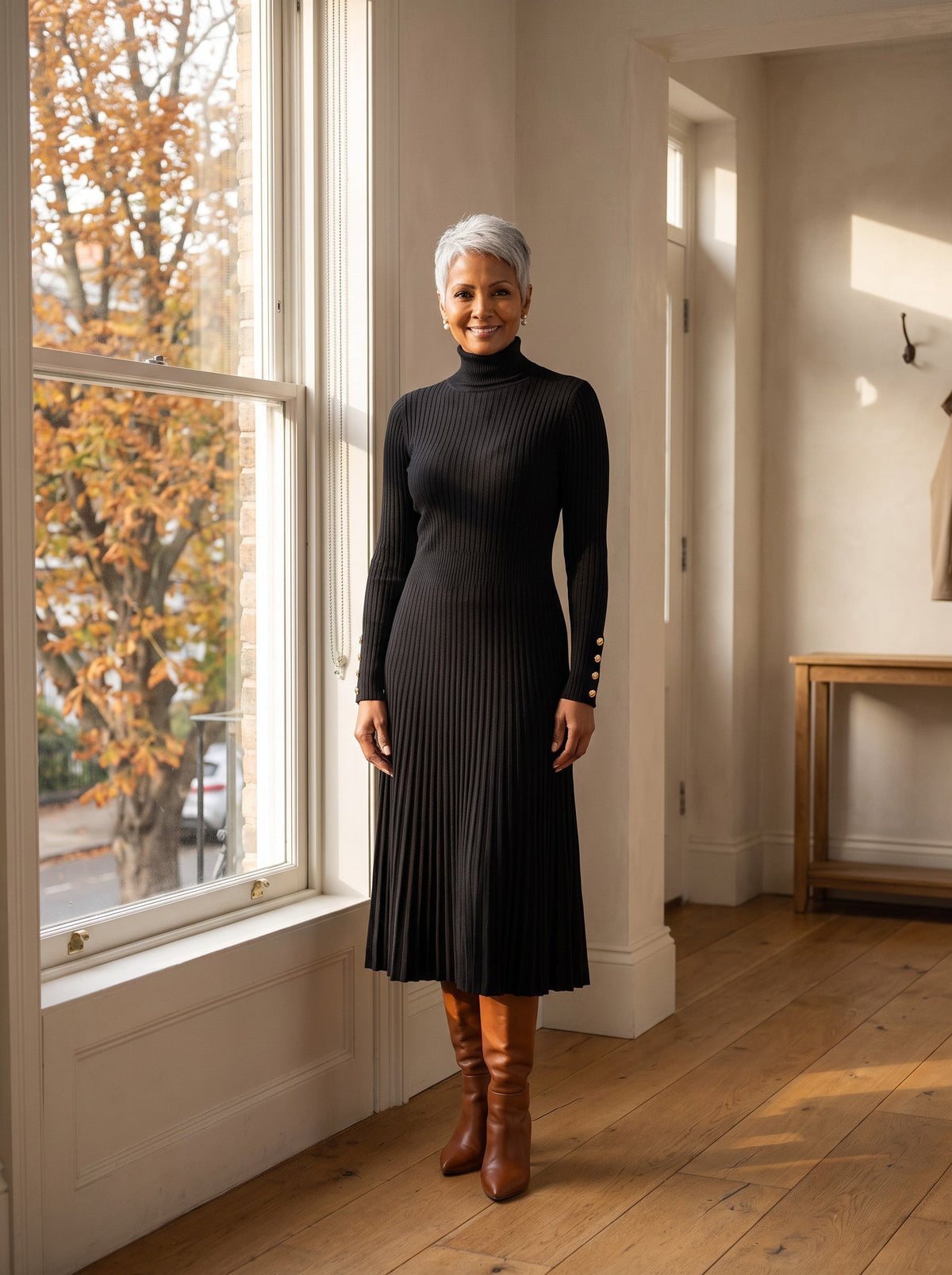 Woman in a black ribbed turtleneck sweater dress and tall boots by a window