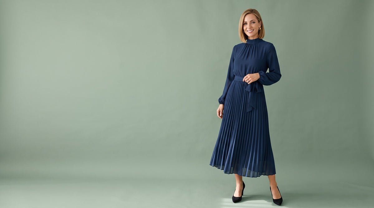 Woman in a navy pleated mock neck midi dress on a sage backdrop